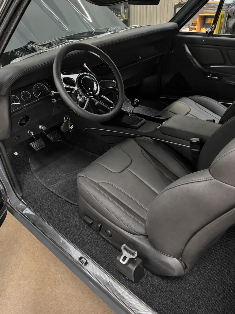 Custom black interior of a restored 1967 Chevrolet Chevelle with bucket seats, updated gauges, a center console, and manual shifter.
